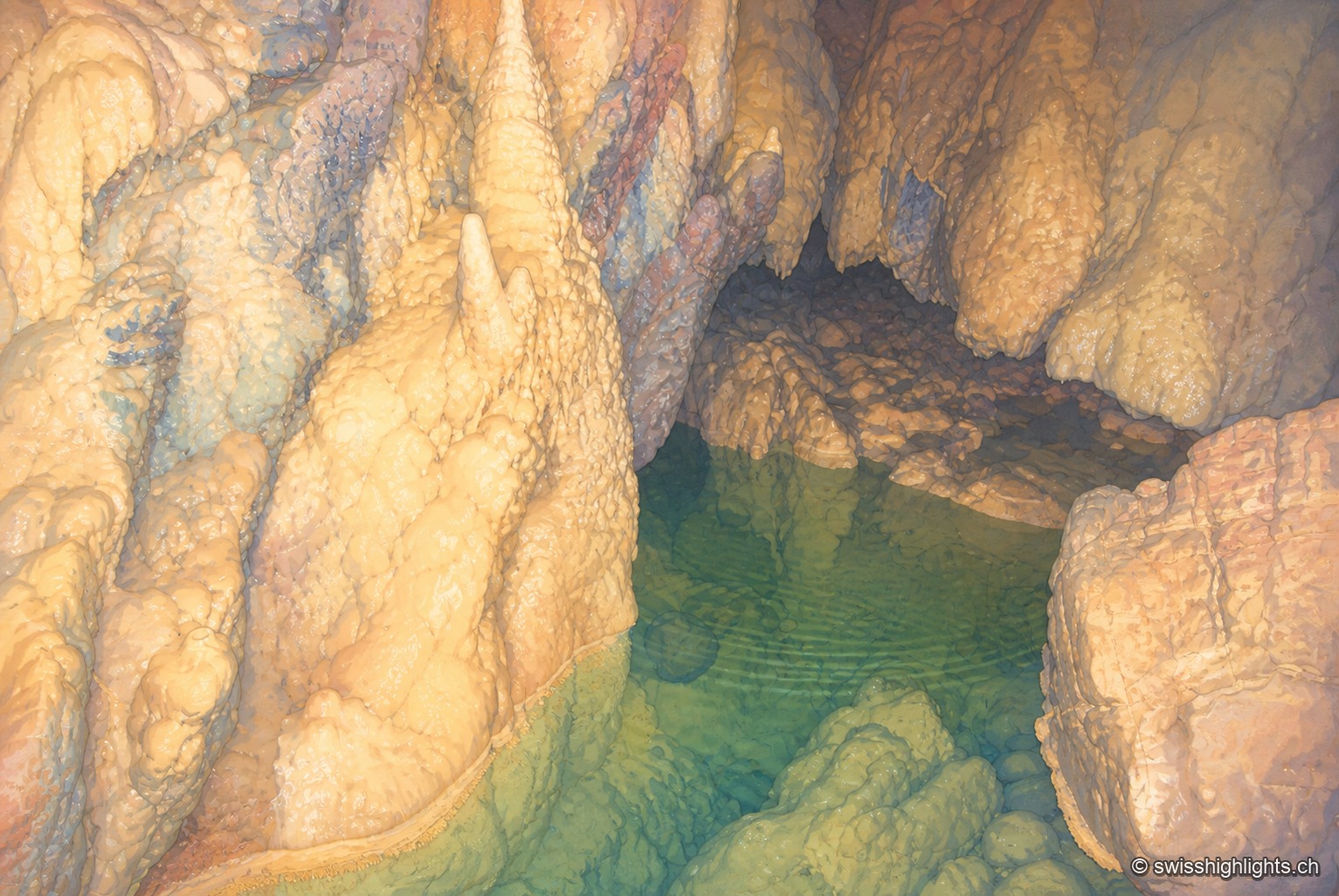 Un lac souterrain aux eaux vert émeraude occupe le creux d'une salle rocheuse, cerné de parois de calcaire sculptées par l'érosion, sous un éclairage discret qui fait scintiller la surface de l'eau.