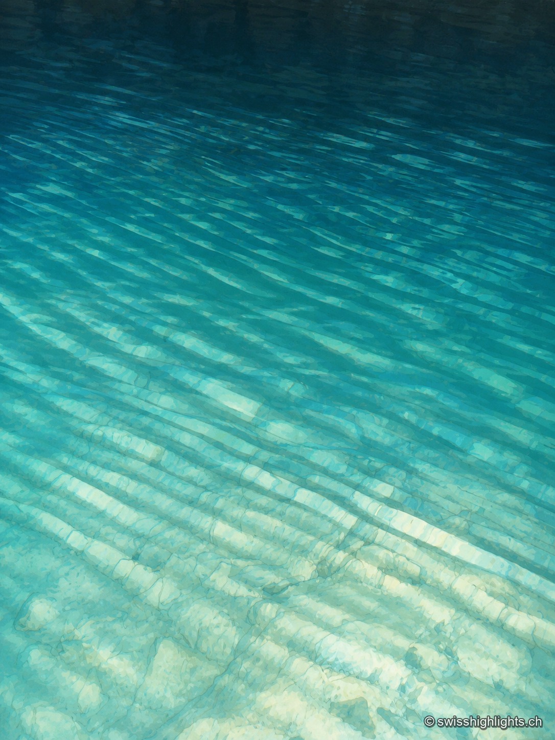 Cadrage vertical en plein cadre sur l'eau turquoise du lac souterrain : des ondulations diagonales et des bandes de lumière caustique traversent la surface, laissant deviner par transparence le fond rocheux strié qui plonge en profondeur.